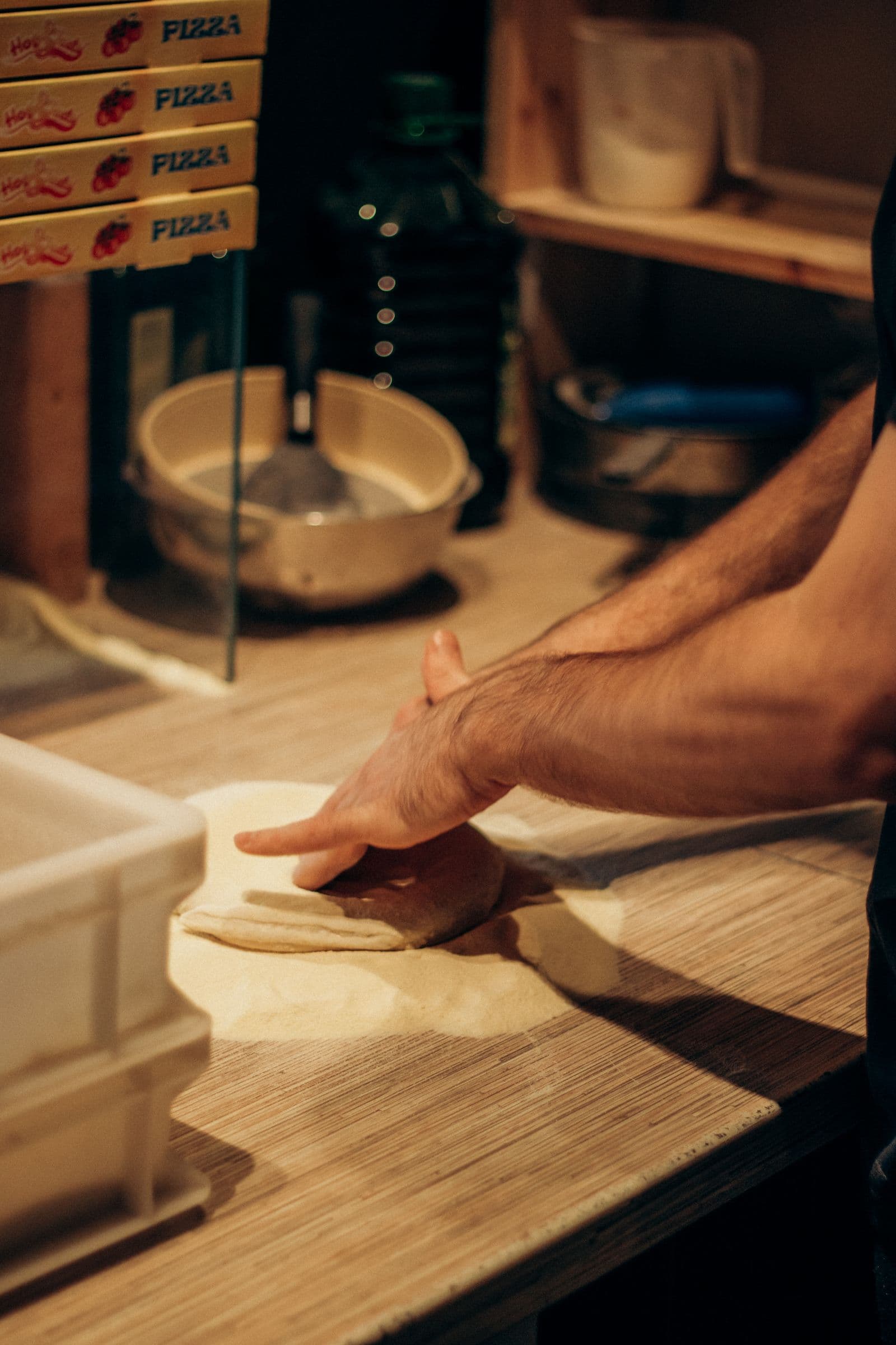 Hands pressing out pizza dough on a floured wooden bench