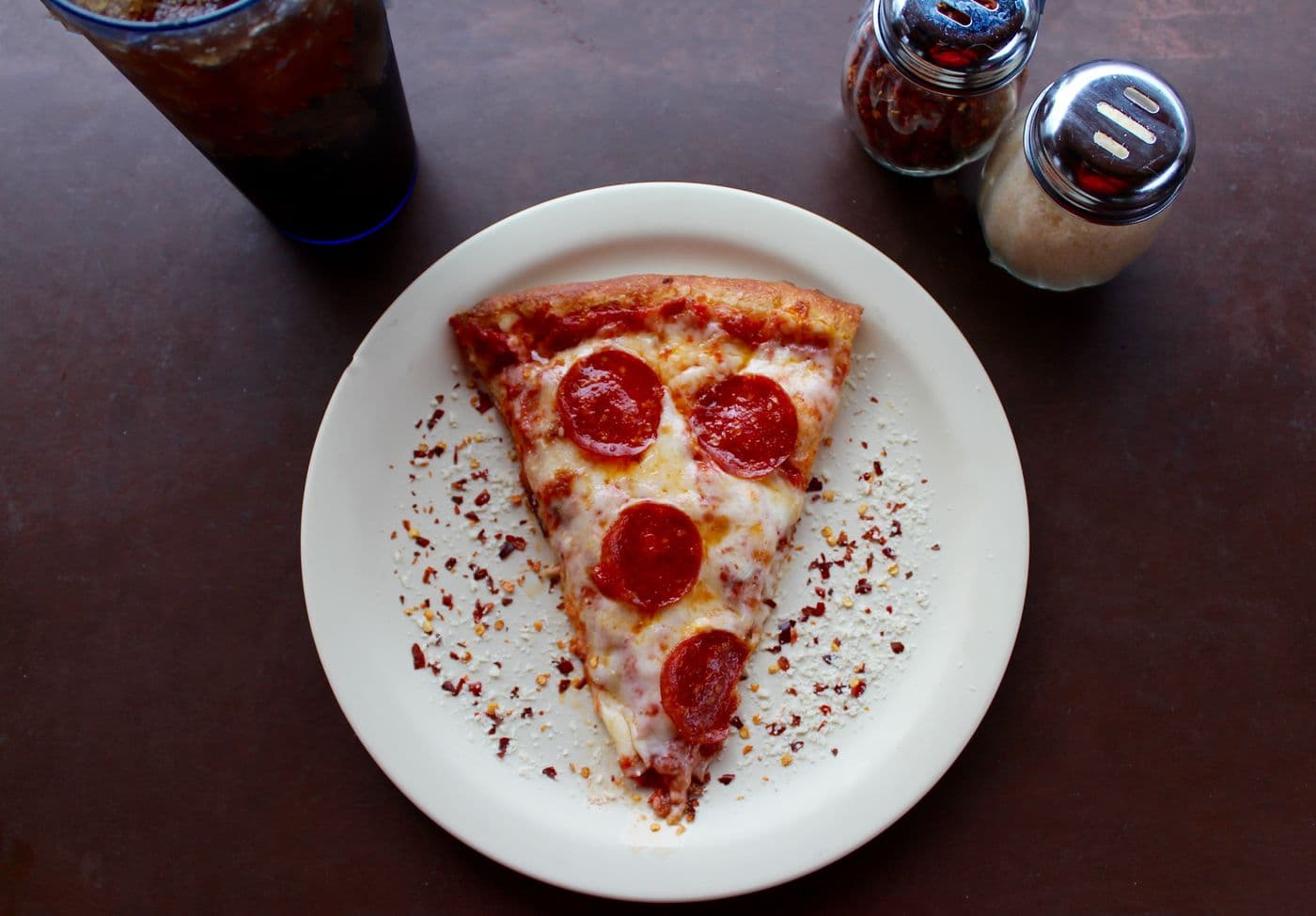 A pepperoni slice on a plate with a soda and shakers