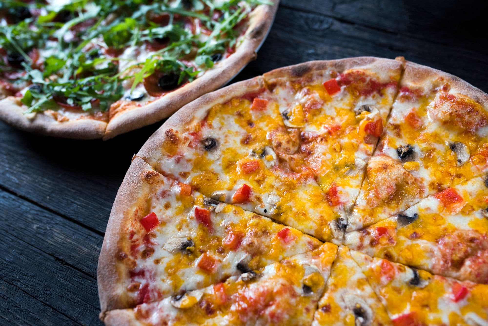 Two freshly baked pizzas on a dark wood table