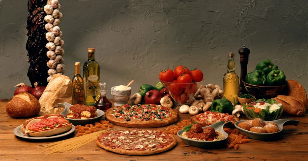 Thin crust pizza, pasta and a hot sub on a wood table