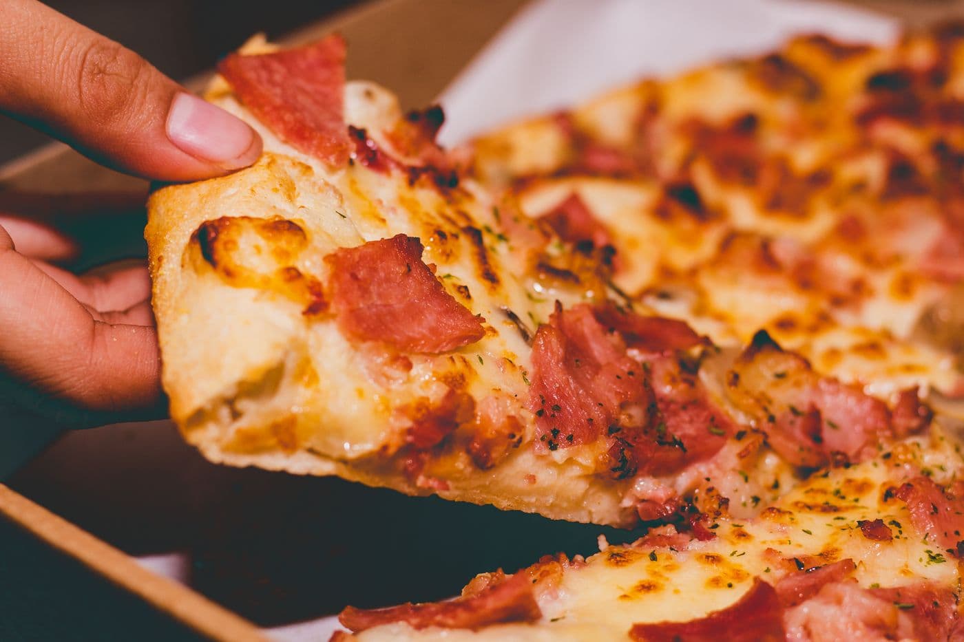 A hand lifting a cheesy slice away from the pie
